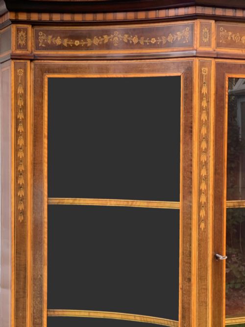 fig 1. An inlaid mahogany display cabinet featuring a swan-neck pediment, glazed upper doors, a mirror-backed central alcove, and detailed floral marquetry on the lower cupboard doors.