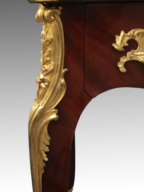 fig 2. A French Louis XV style bureau plat crafted from dark polished wood with serpentine cabriole legs, elaborate gilt-bronze ormolu mounts, and a black leather writing top.