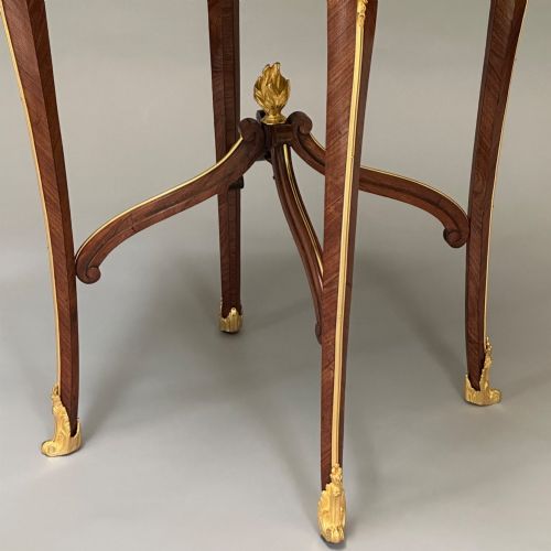 fig 1. A round French kingwood occasional table featuring floral marquetry inlay, gilded ormolu mounts, slender cabriole legs, and a central stretcher with a carved finial.