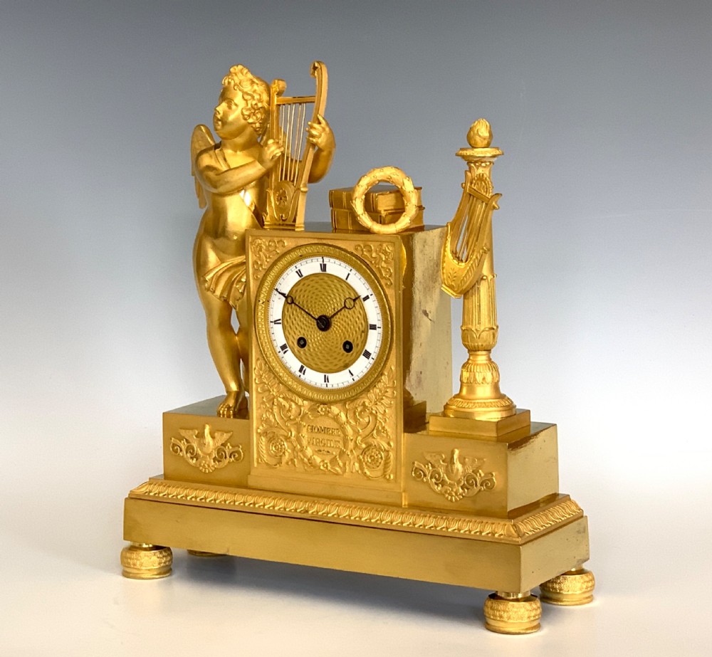 A 19th-century French Empire gilt bronze mantel clock featuring a cherub figure holding a lyre alongside classical decorative elements. View V