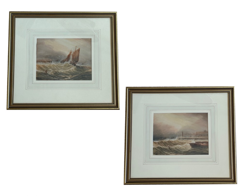 A pair of framed Edwardian watercolour paintings depicting stormy seas, one with a sailing vessel and the other featuring a coastal lighthouse.