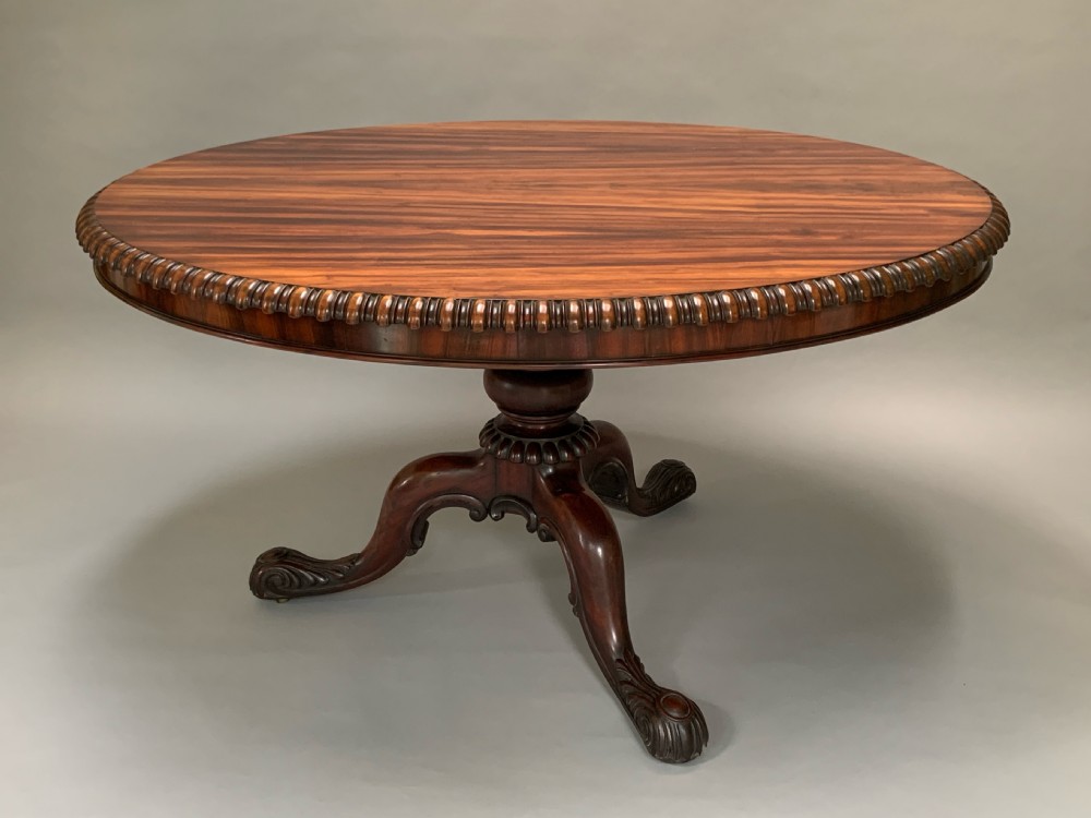 An oval William IV centre table in highly figured Albuera wood featuring a gadrooned rim and a carved pedestal base with scrolled feet.