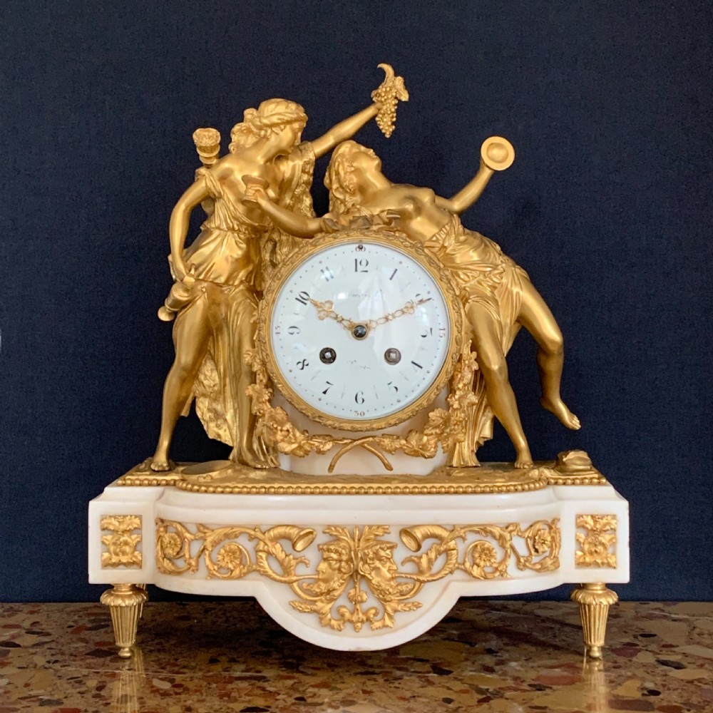 A Louis XVI style French ormolu and white marble mantel clock depicting two sculptural classical female figures flanking a circular white enamel dial.