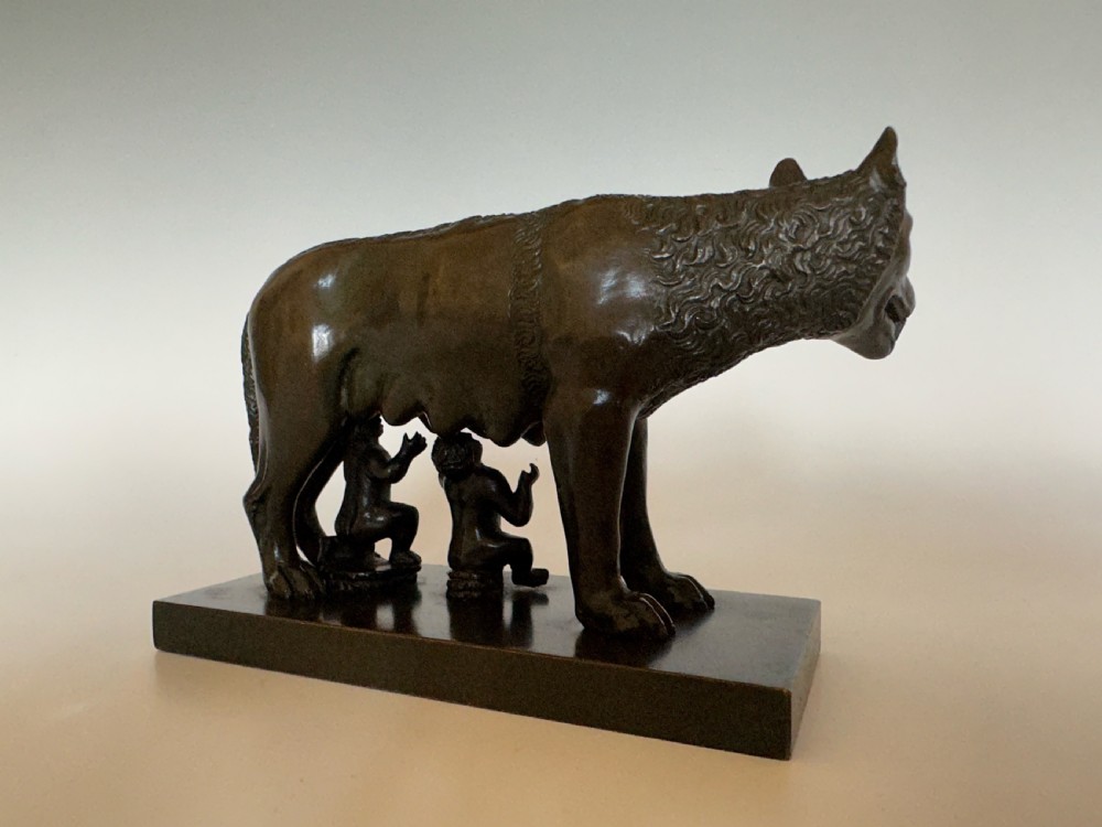 A dark bronze sculpture depicting the Capitoline Wolf nursing Romulus and Remus on a rectangular bronze base. View II