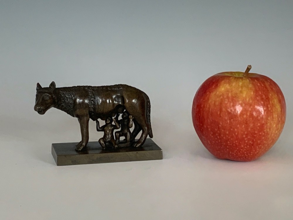 A dark bronze sculpture depicting the Capitoline Wolf nursing Romulus and Remus on a rectangular bronze base. View IV