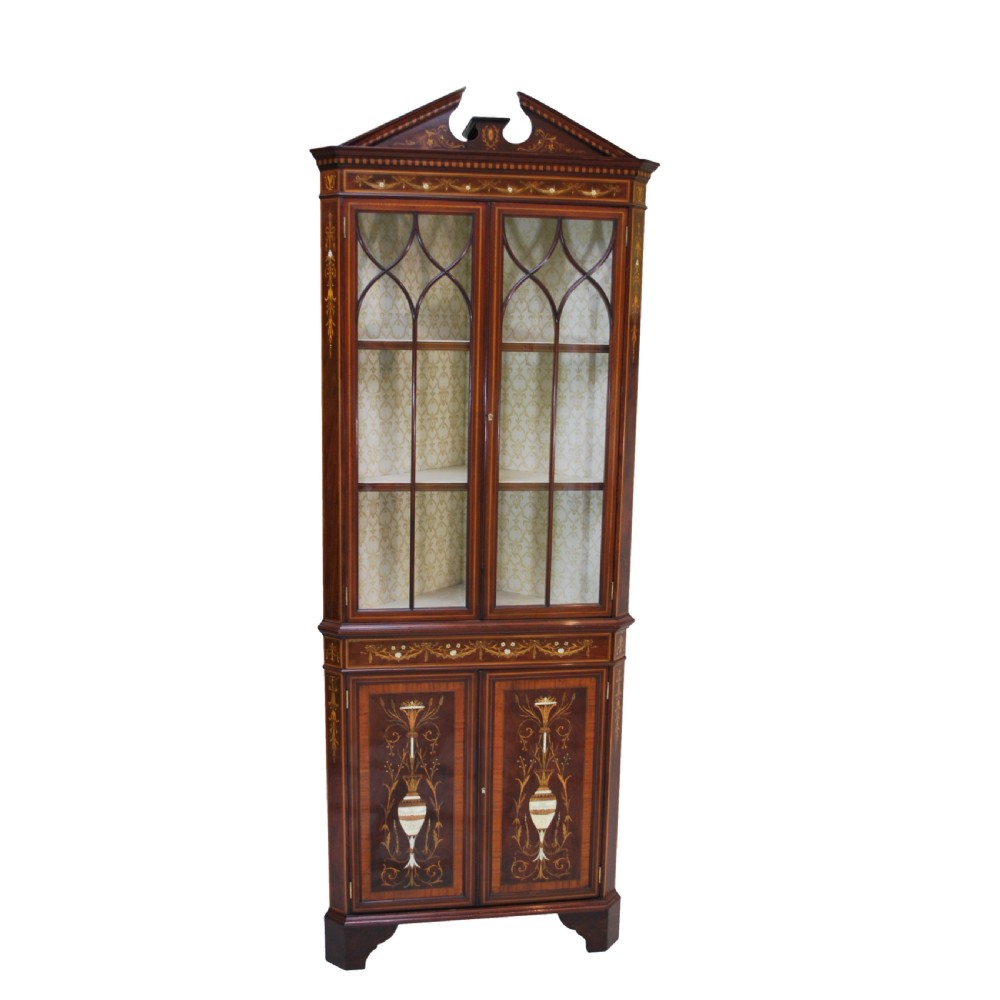 A tall late Victorian mahogany corner cabinet featuring a broken arch pediment, astragal glazed upper doors, and inlaid lower cupboard doors.