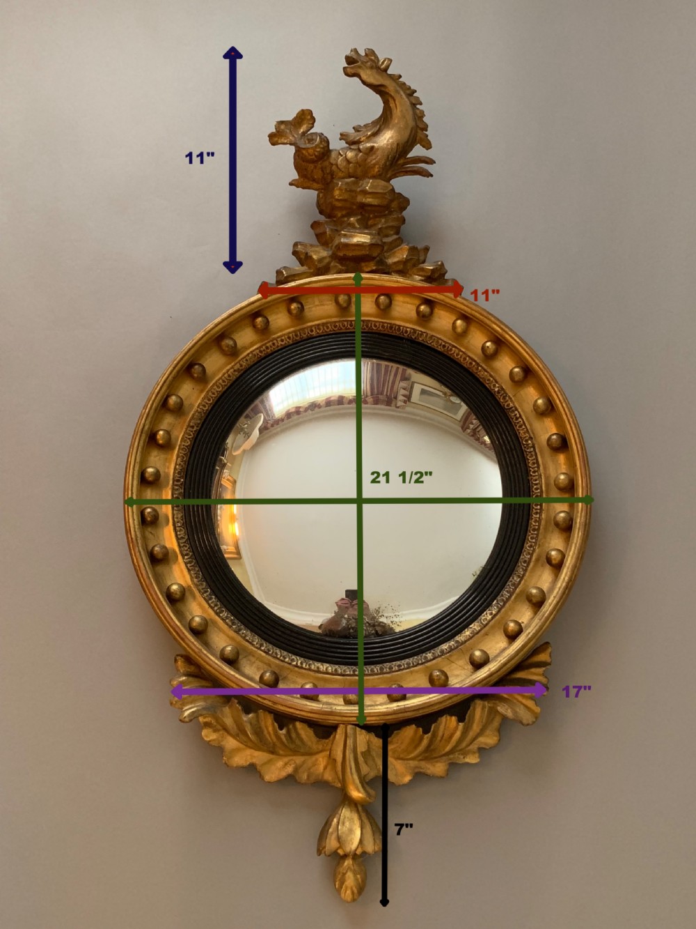 A circular Regency giltwood convex mirror with a ball-studded frame, an ebonised inner ring, an elaborate carved creature cresting, and an acanthus leaf apron. View II