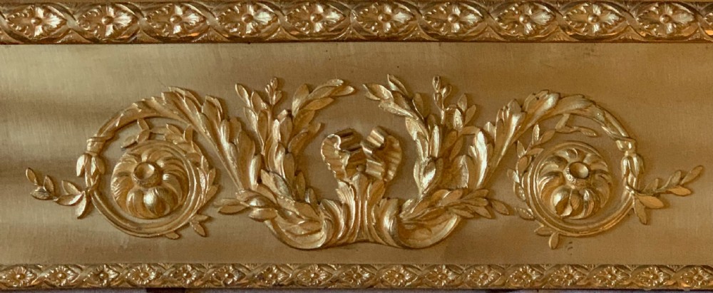 A rectangular gold-coloured brass fireplace inset surround featuring detailed neoclassical relief appliques including torches, foliate scrolls, and beaded borders. View V