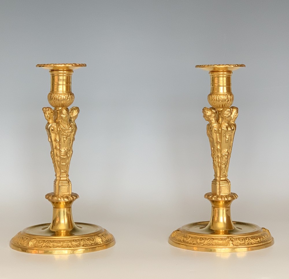 A pair of French Regence gilt bronze candlesticks featuring tapered columns decorated with allegorical term busts and circular chased bases.