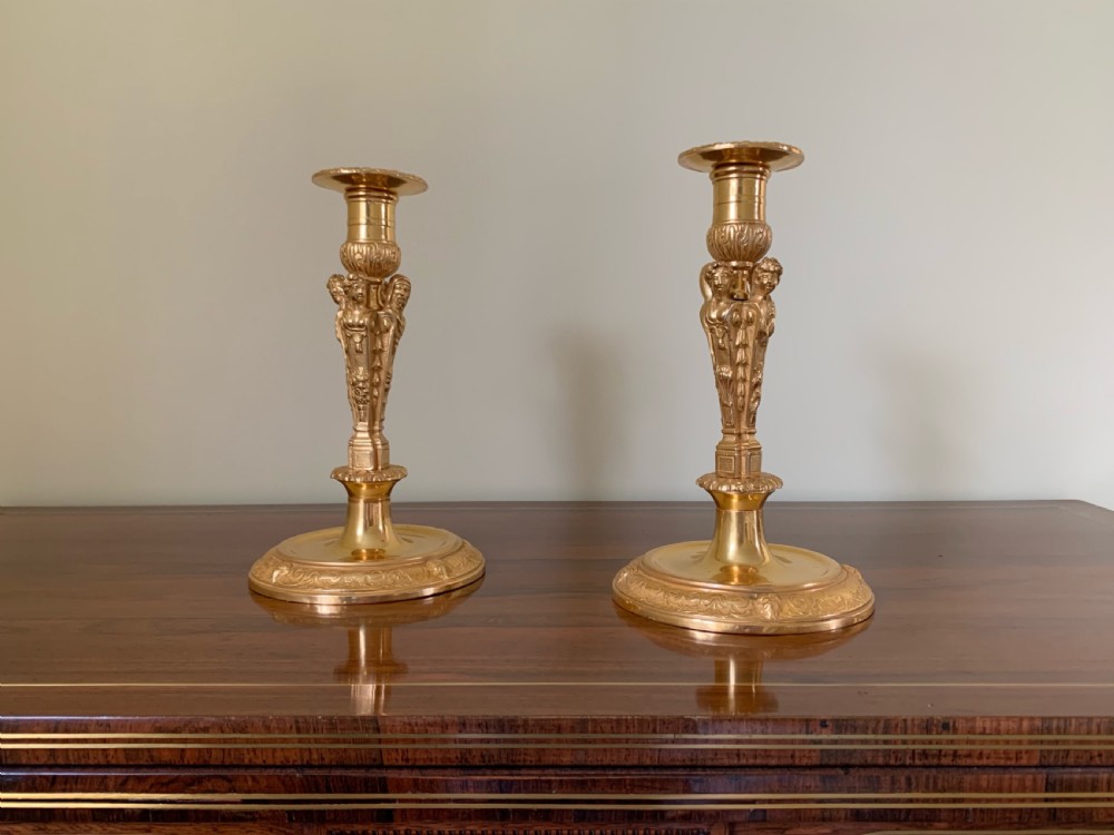 A pair of French Regence gilt bronze candlesticks featuring tapered columns decorated with allegorical term busts and circular chased bases. View IX