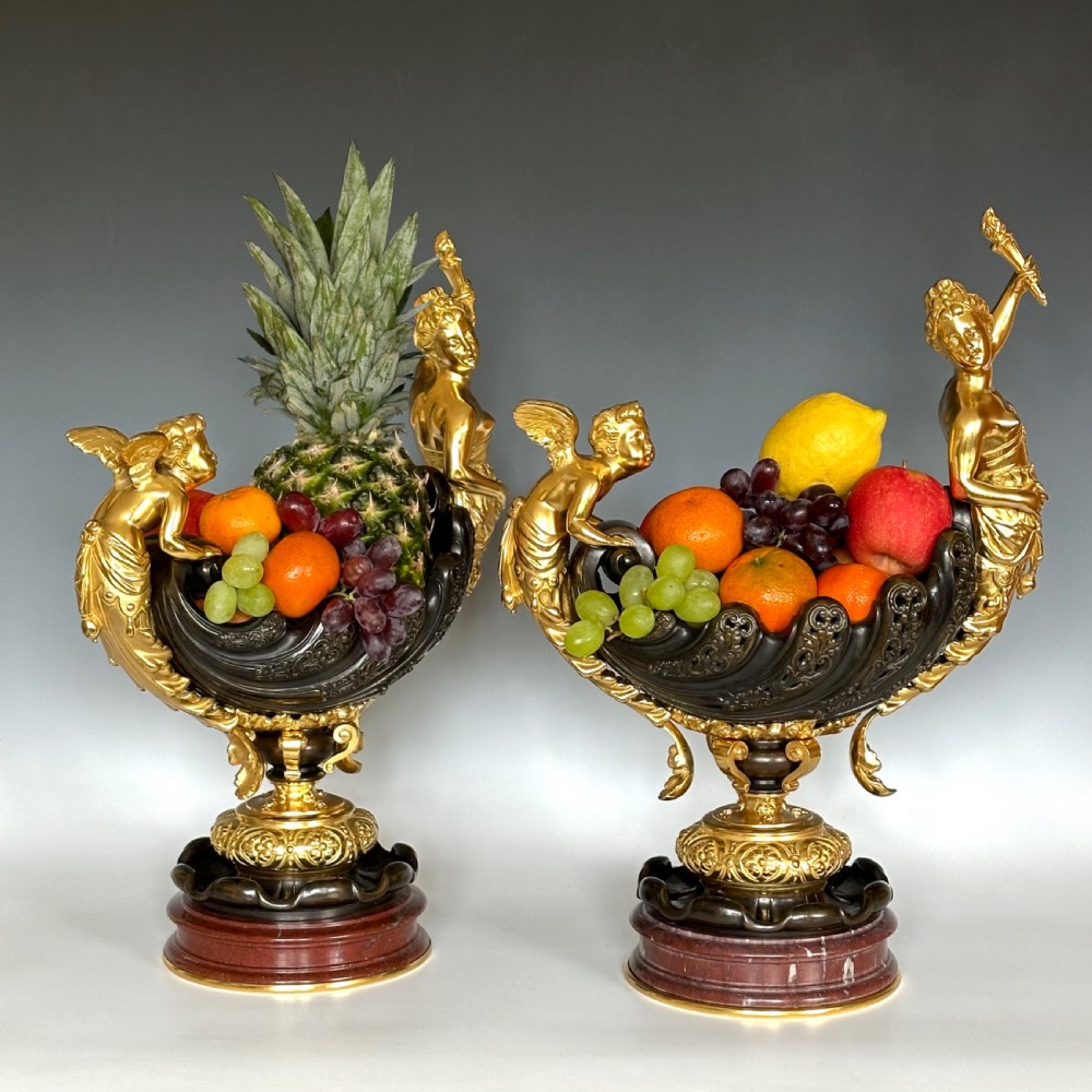 A pair of antique French ormolu and patinated bronze centrepieces featuring sculpted winged figures and cherubs on circular red marble bases. View II