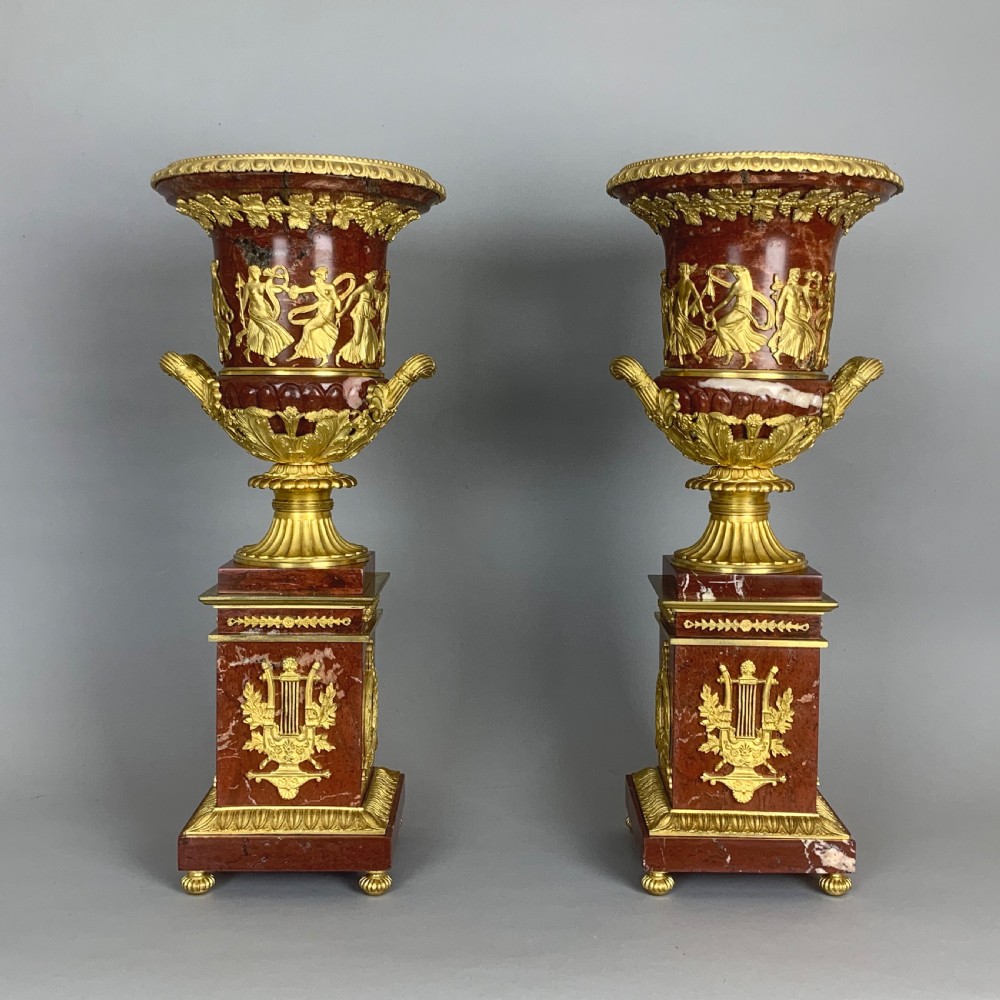 A pair of red marble urns featuring gilt bronze mounts, classical relief friezes of dancing figures, and pedestal bases decorated with lyres. View VI