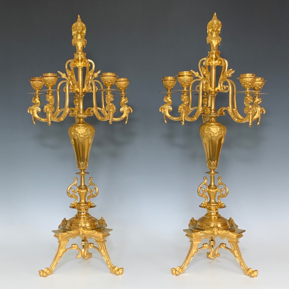 A pair of antique French ormolu five-branch candelabra featuring scrollwork arms, classical urn stems, and a gilded finish.
