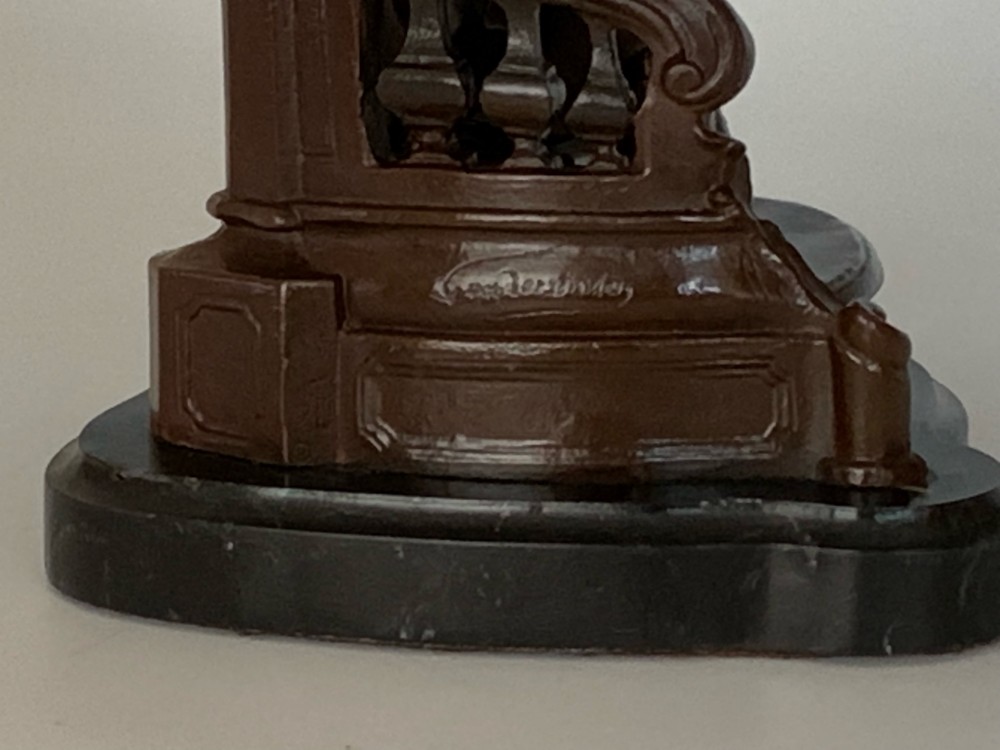 A patinated dark bronze sculpture of a woman in period dress standing on steps with a balustrade mounted on a dark marble base. View VI