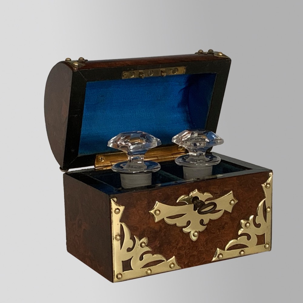 An open Victorian burr walnut scent casket with brass corner mounts containing two cut glass perfume bottles lined with blue fabric.