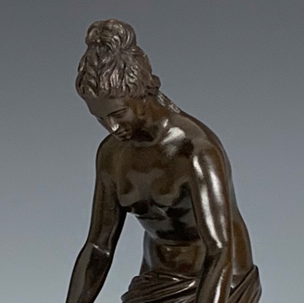 A dark brown patinated bronze figure depicting a draped female classical figure leaning over a small pedestal basin, mounted on a round base. View VII