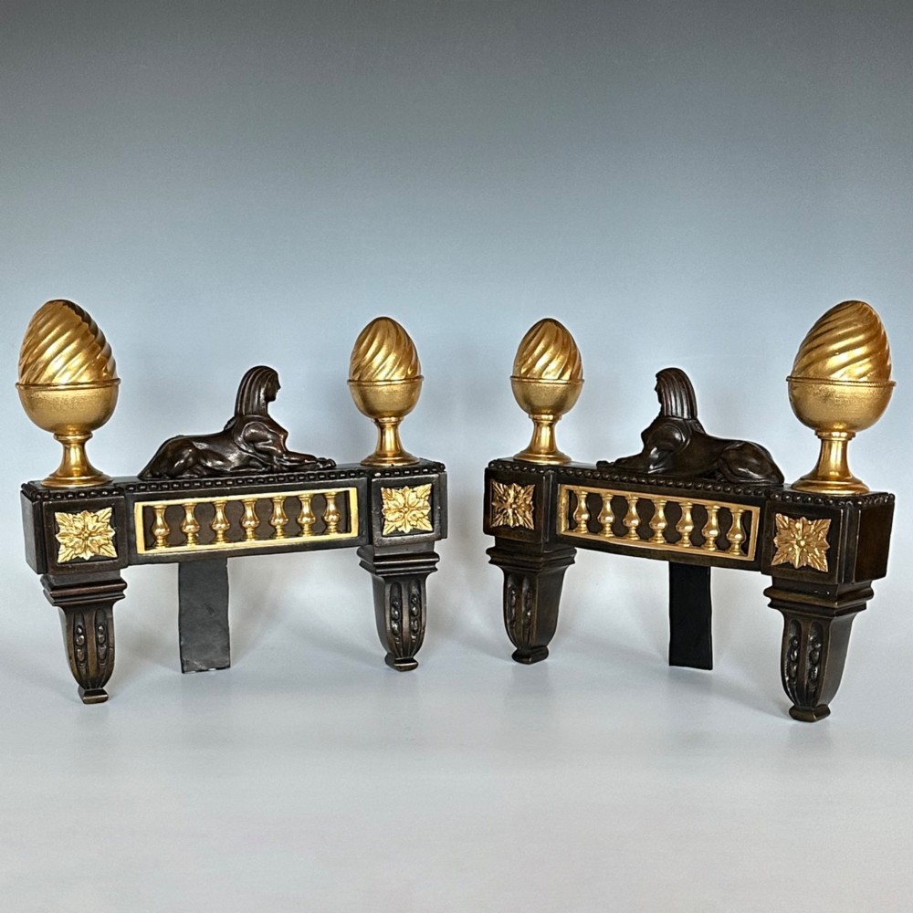 A pair of Regency bronze and ormolu chenets featuring sculpted bronze sphinxes, gilded balustrades, pinecone finials, and fluted legs. View IV