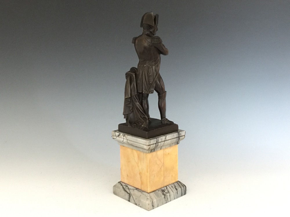 A nineteenth-century bronze figure of Napoleon Bonaparte in full military uniform standing with arms crossed on a yellow and grey marble plinth. View V