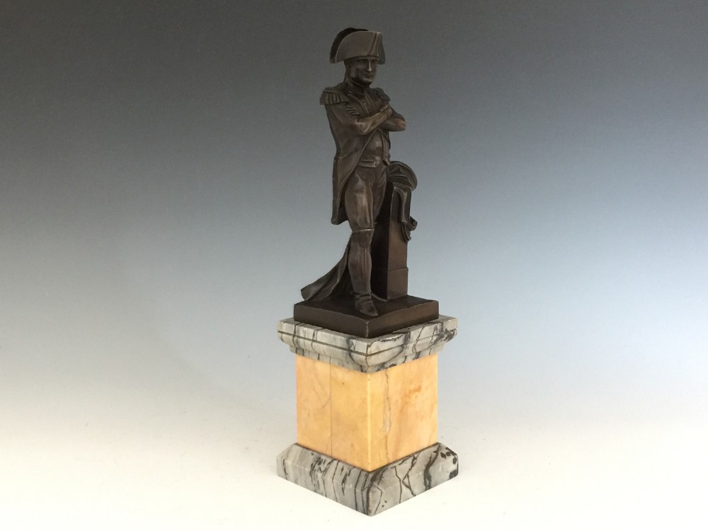 A nineteenth-century bronze figure of Napoleon Bonaparte in full military uniform standing with arms crossed on a yellow and grey marble plinth. View VI