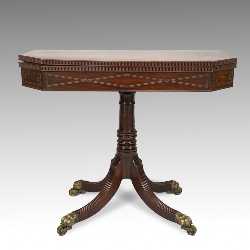 A George IV mahogany fold-over card table featuring a turned pedestal stem, geometric frieze inlay, and splayed legs with brass paw castors.