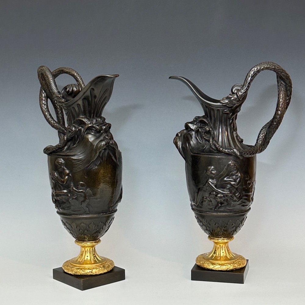 A pair of dark patinated bronze French ewers featuring relief carvings of classical mythological figures, serpent handles, satyr masks, and gilt bronze bases. View II