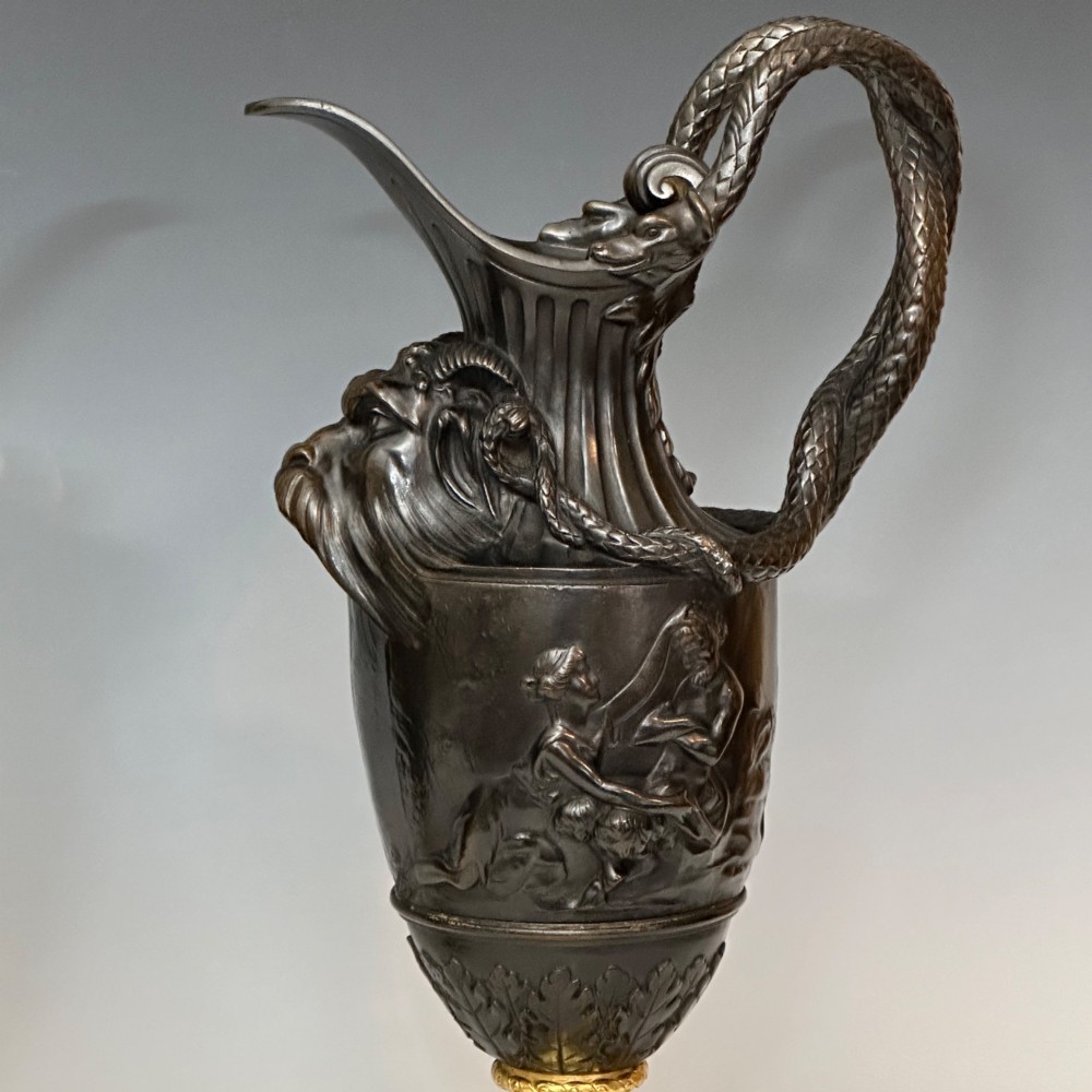 A pair of dark patinated bronze French ewers featuring relief carvings of classical mythological figures, serpent handles, satyr masks, and gilt bronze bases. View III