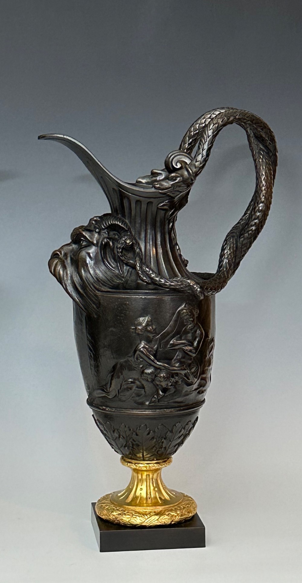 A pair of dark patinated bronze French ewers featuring relief carvings of classical mythological figures, serpent handles, satyr masks, and gilt bronze bases. View IV