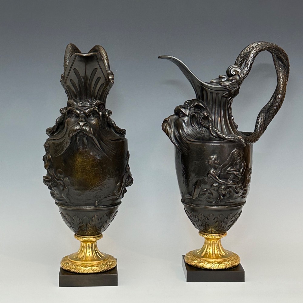 A pair of dark patinated bronze French ewers featuring relief carvings of classical mythological figures, serpent handles, satyr masks, and gilt bronze bases. View V