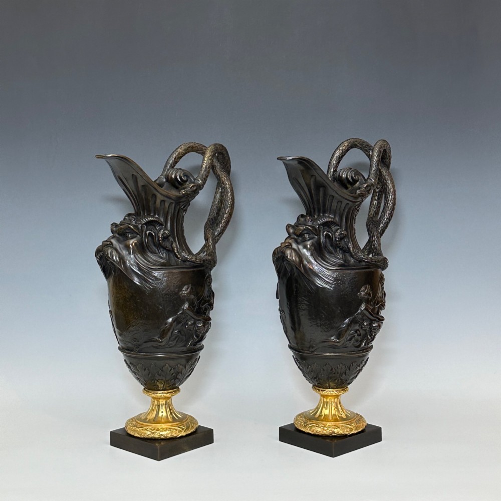 A pair of dark patinated bronze French ewers featuring relief carvings of classical mythological figures, serpent handles, satyr masks, and gilt bronze bases. View VI