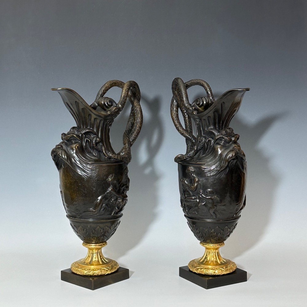 A pair of dark patinated bronze French ewers featuring relief carvings of classical mythological figures, serpent handles, satyr masks, and gilt bronze bases. View IX
