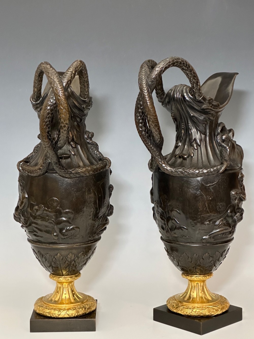 A pair of dark patinated bronze French ewers featuring relief carvings of classical mythological figures, serpent handles, satyr masks, and gilt bronze bases. View XI