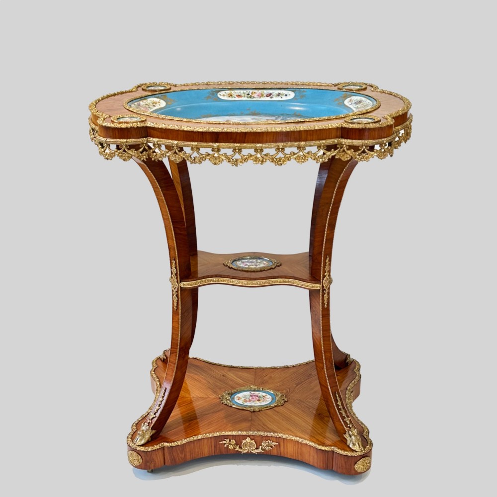 A French Napoleon III tulipwood gueridon featuring gilt-bronze mounts, a central blue Sevres-style porcelain top plaque, and two tiered shelves. View II