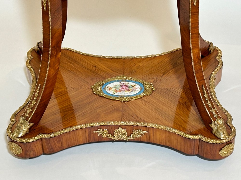 A French Napoleon III tulipwood gueridon featuring gilt-bronze mounts, a central blue Sevres-style porcelain top plaque, and two tiered shelves. View III