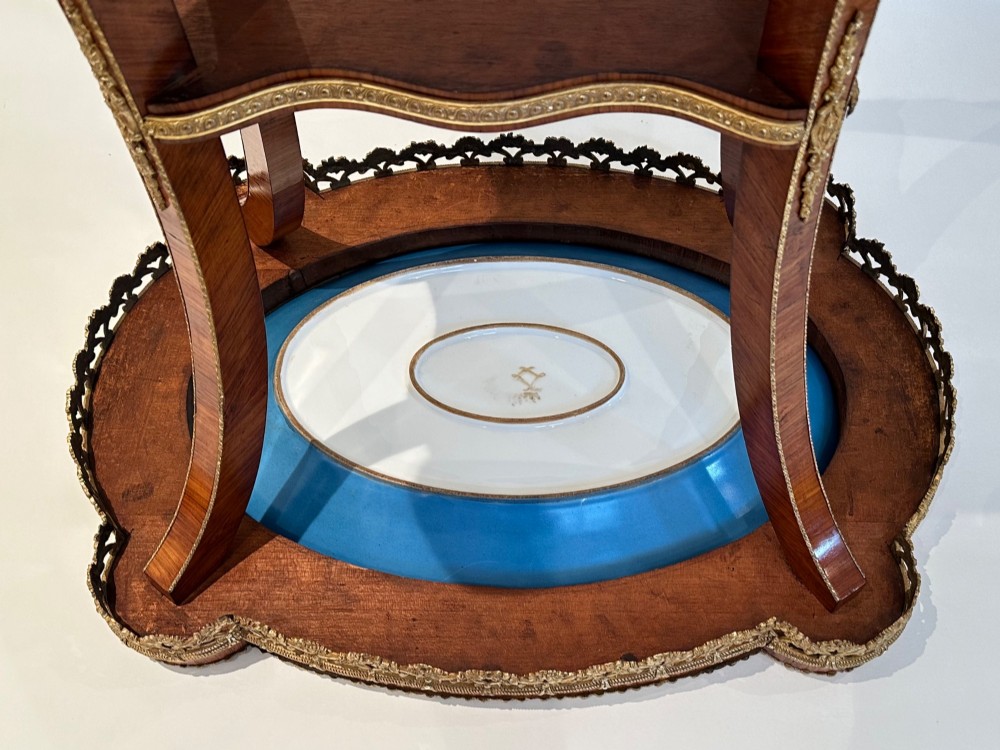 A French Napoleon III tulipwood gueridon featuring gilt-bronze mounts, a central blue Sevres-style porcelain top plaque, and two tiered shelves. View IV