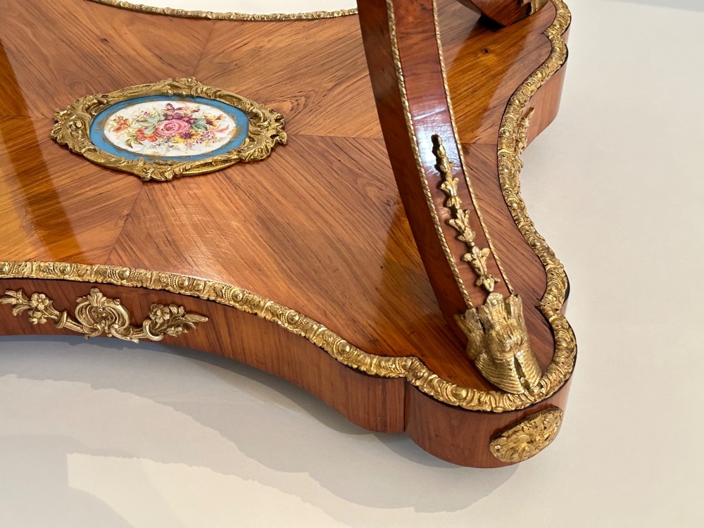 A French Napoleon III tulipwood gueridon featuring gilt-bronze mounts, a central blue Sevres-style porcelain top plaque, and two tiered shelves. View V