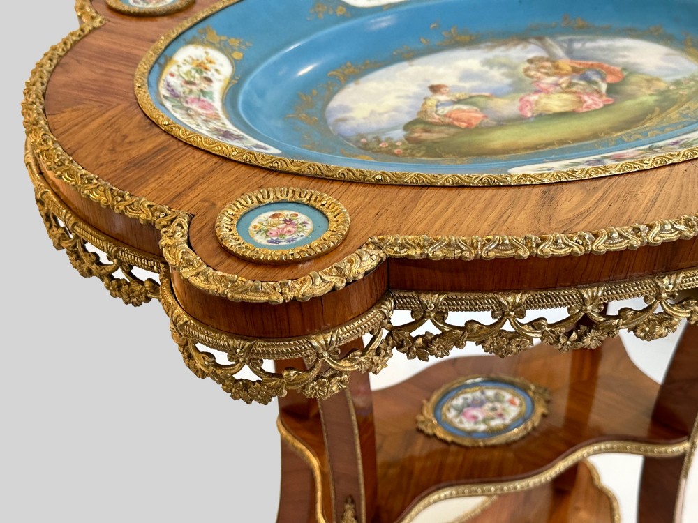 A French Napoleon III tulipwood gueridon featuring gilt-bronze mounts, a central blue Sevres-style porcelain top plaque, and two tiered shelves. View VI