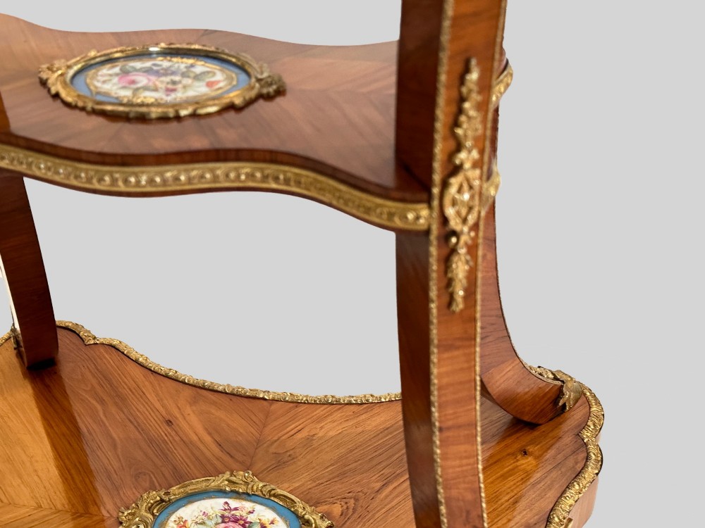 A French Napoleon III tulipwood gueridon featuring gilt-bronze mounts, a central blue Sevres-style porcelain top plaque, and two tiered shelves. View VII