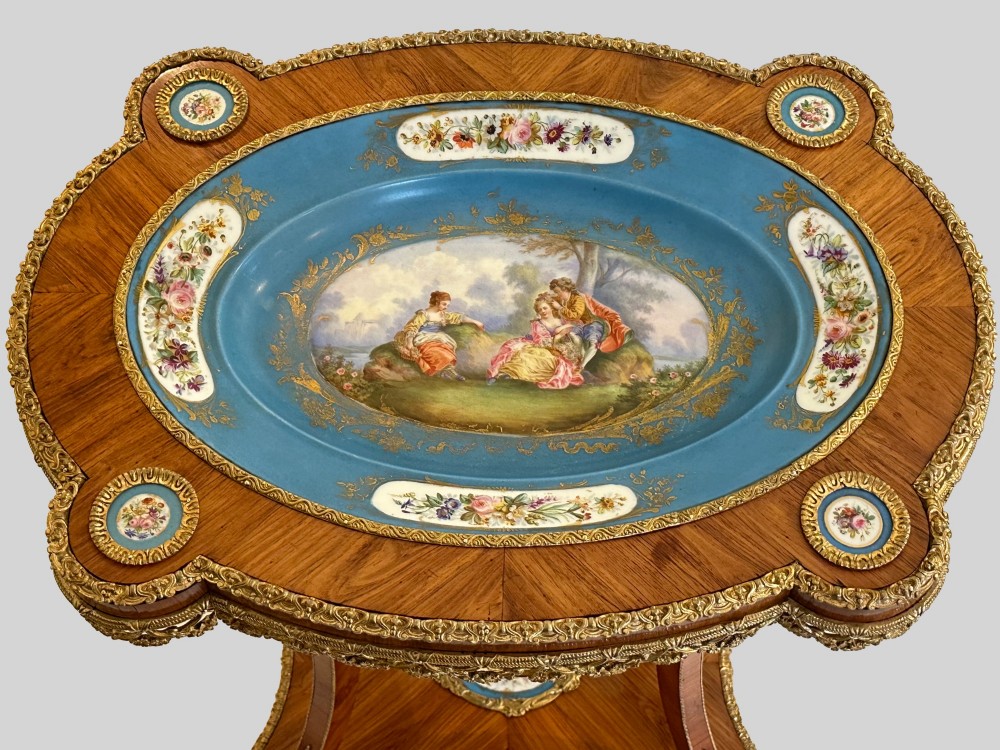 A French Napoleon III tulipwood gueridon featuring gilt-bronze mounts, a central blue Sevres-style porcelain top plaque, and two tiered shelves. View VIII