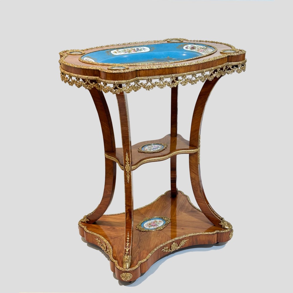 A French Napoleon III tulipwood gueridon featuring gilt-bronze mounts, a central blue Sevres-style porcelain top plaque, and two tiered shelves. View X