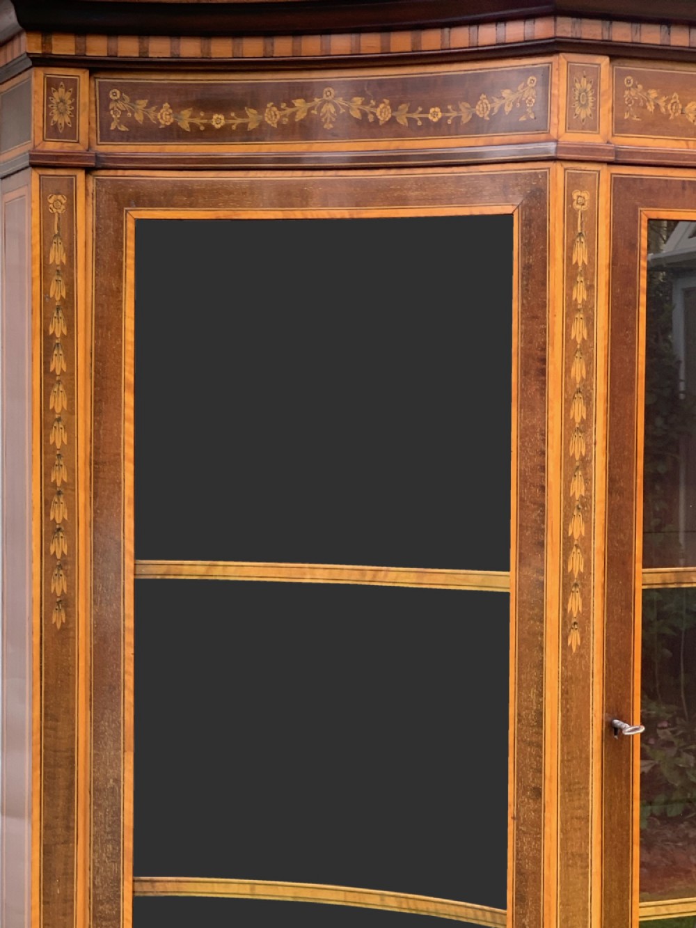 An inlaid mahogany display cabinet featuring a swan-neck pediment, glazed upper doors, a mirror-backed central alcove, and detailed floral marquetry on the lower cupboard doors. View II