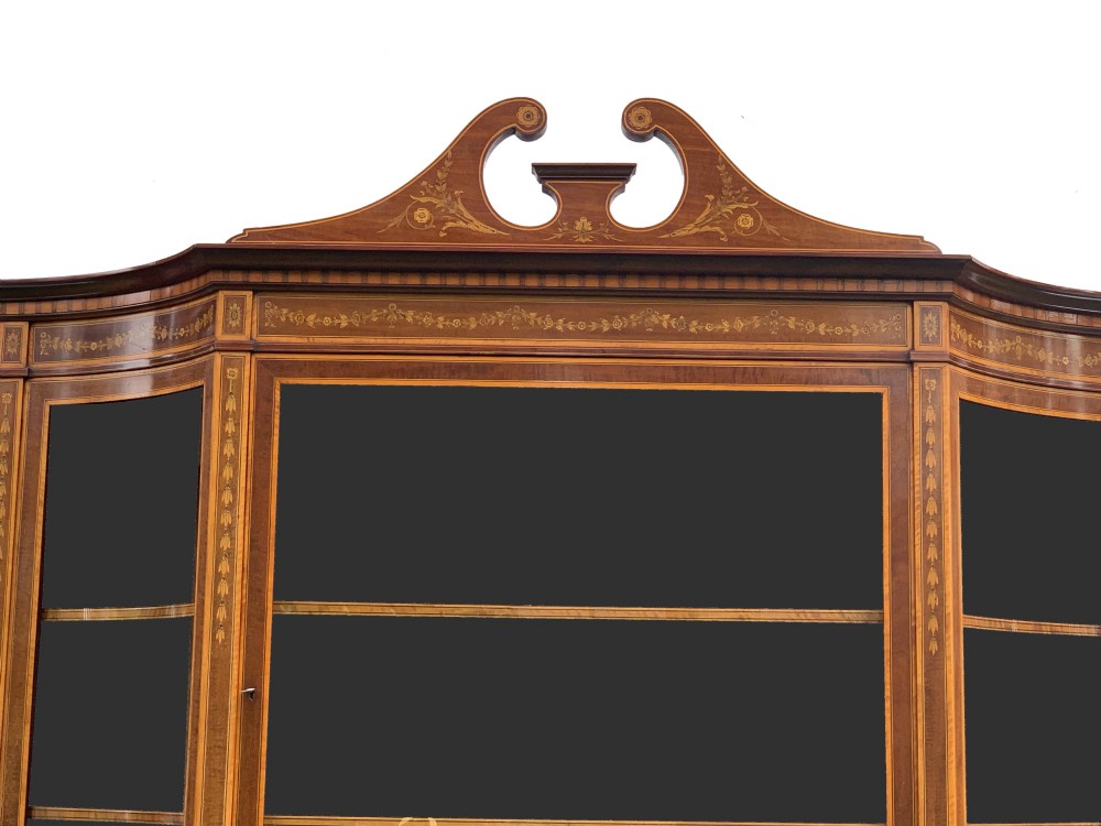 An inlaid mahogany display cabinet featuring a swan-neck pediment, glazed upper doors, a mirror-backed central alcove, and detailed floral marquetry on the lower cupboard doors. View VI