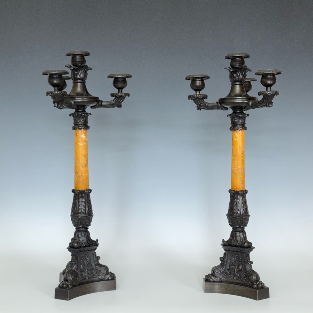 A pair of French Restoration period dark bronze candelabra with four candle branches each, supported by cylindrical yellow marble columns on detailed cast bronze tripartite bases.