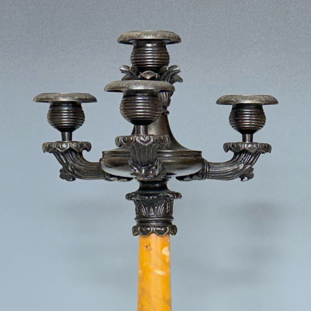 A pair of French Restoration period dark bronze candelabra with four candle branches each, supported by cylindrical yellow marble columns on detailed cast bronze tripartite bases. View II