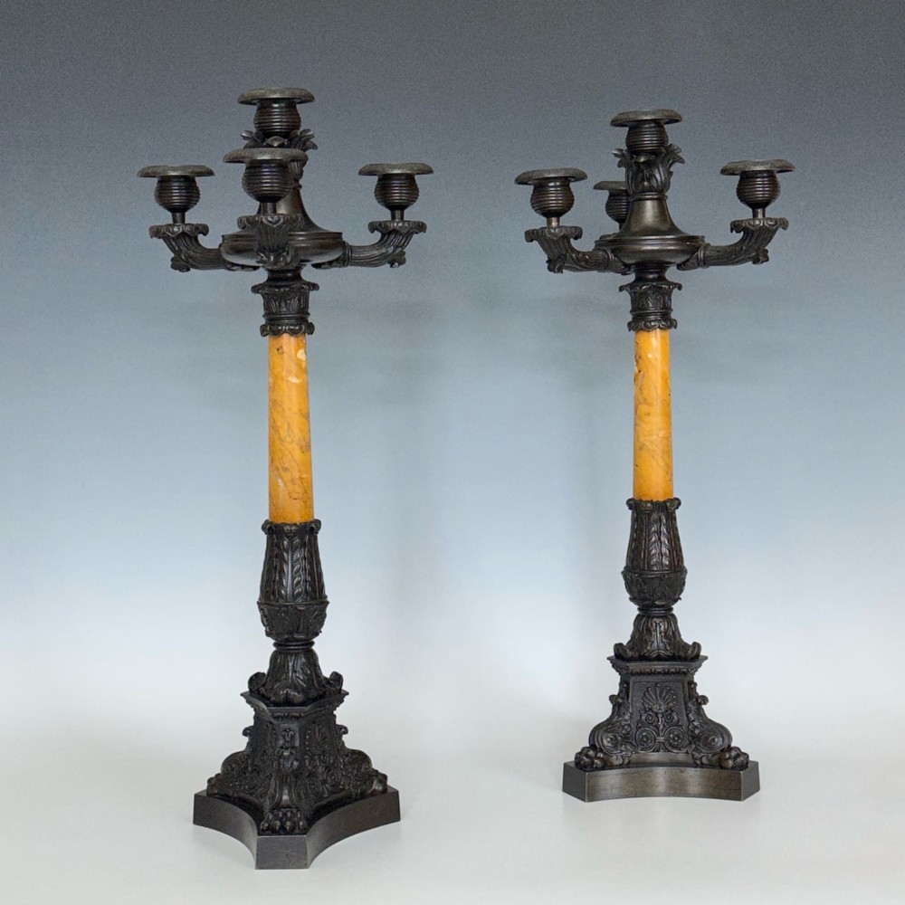 A pair of French Restoration period dark bronze candelabra with four candle branches each, supported by cylindrical yellow marble columns on detailed cast bronze tripartite bases. View VI