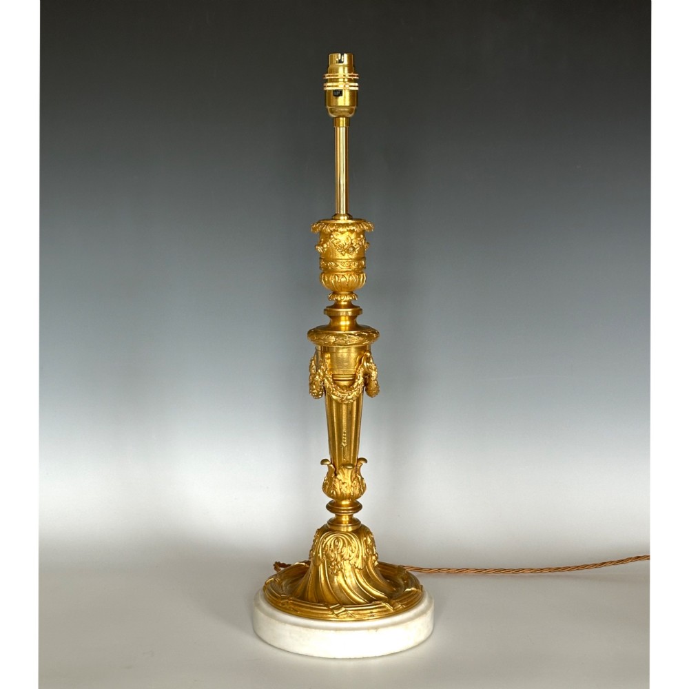 A Louis XV style gilt bronze ormolu table lamp featuring cast foliage swags, acanthus leaf detailing, and a circular white marble base.