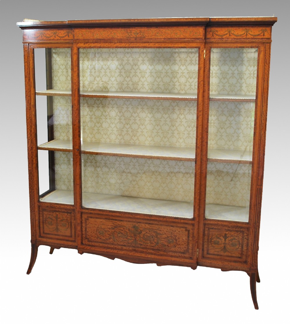 A late Victorian satinwood display cabinet featuring three glazed doors, detailed marquetry inlay, fabric-lined interior shelves, and splayed legs. View III