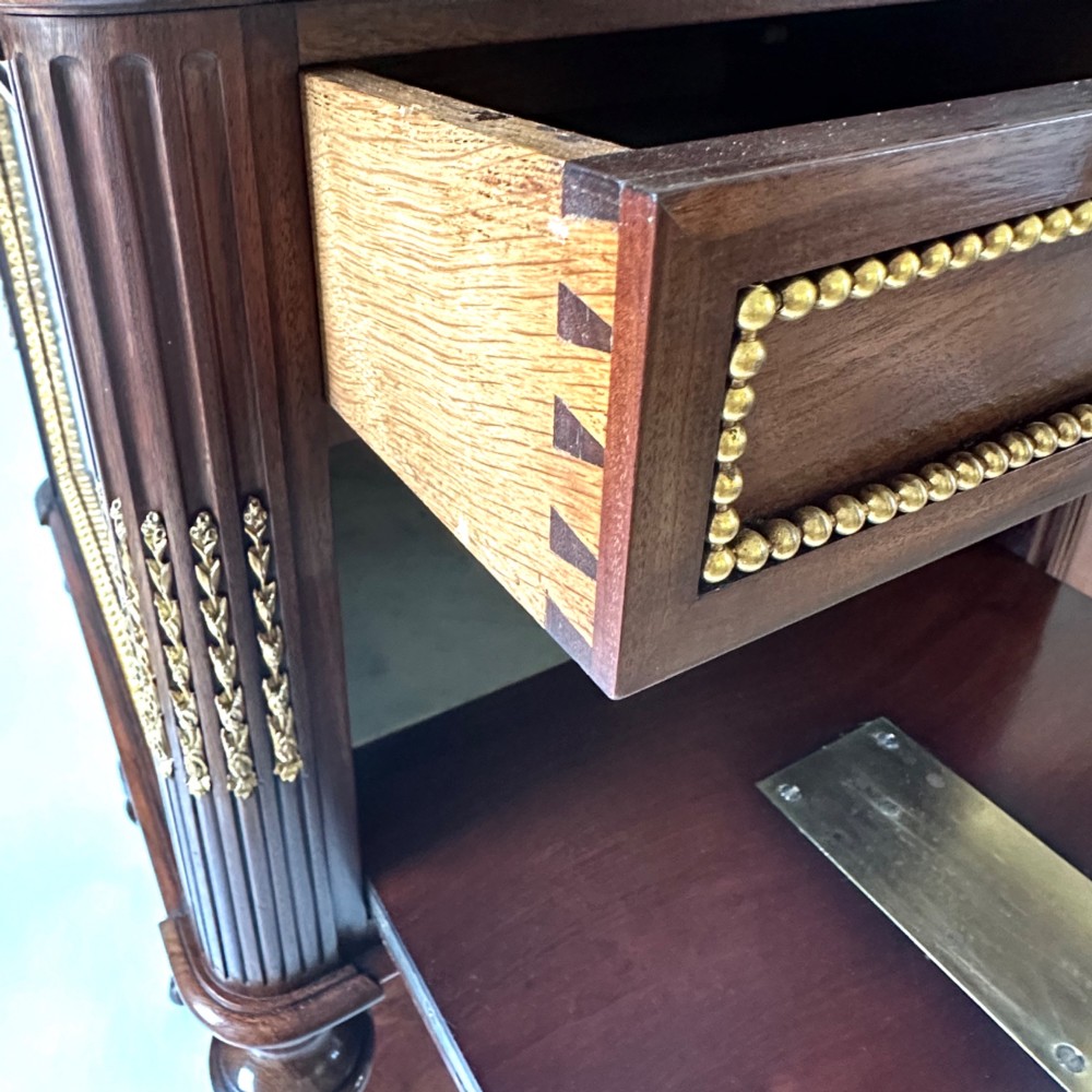 A French Louis XVI style mahogany bedside cabinet featuring two drawers framed with beaded ormolu trim, fluted corner columns, a lower tier shelf, and turned legs with brass castors. View III