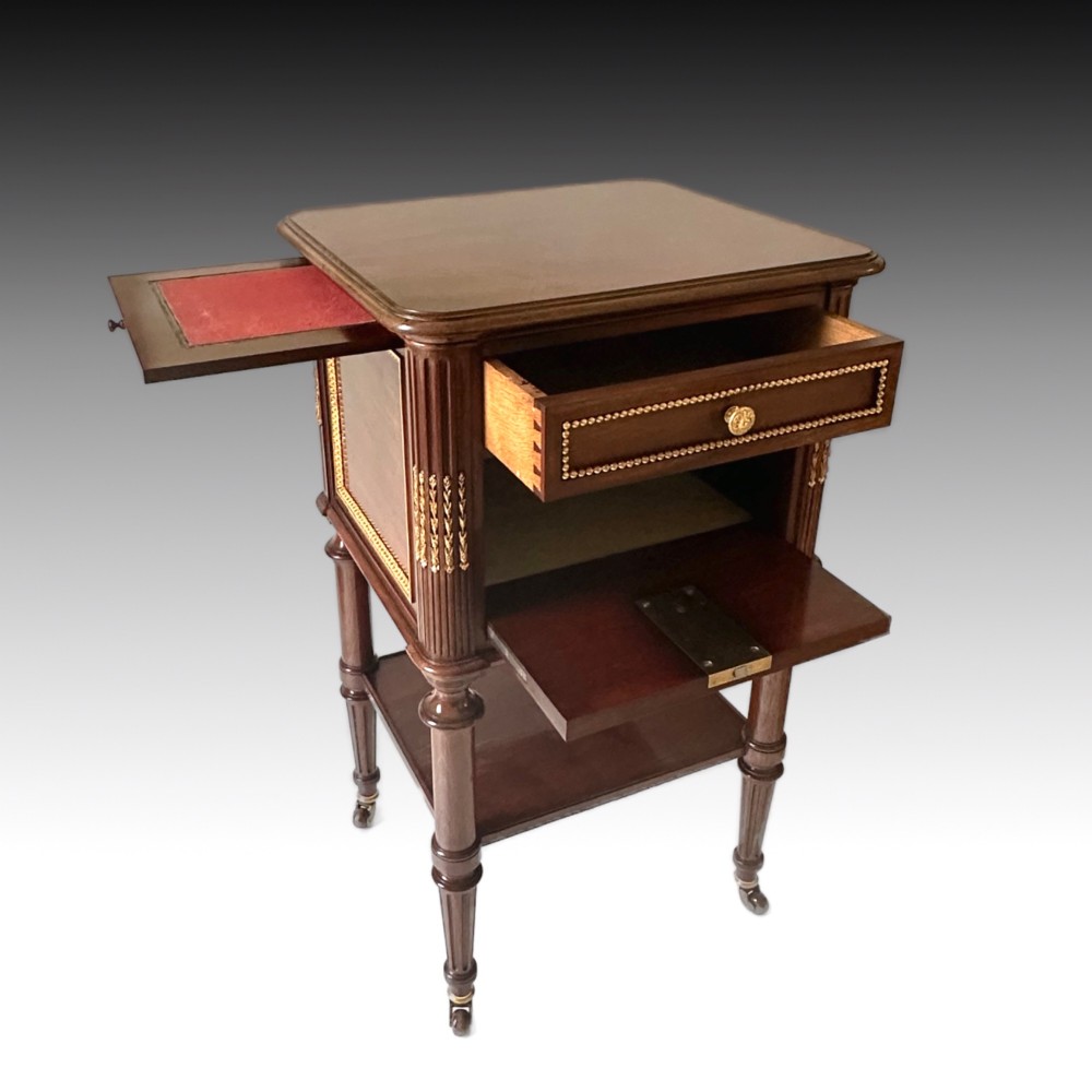 A French Louis XVI style mahogany bedside cabinet featuring two drawers framed with beaded ormolu trim, fluted corner columns, a lower tier shelf, and turned legs with brass castors. View IV