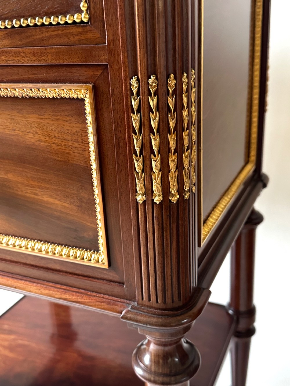 A French Louis XVI style mahogany bedside cabinet featuring two drawers framed with beaded ormolu trim, fluted corner columns, a lower tier shelf, and turned legs with brass castors. View V