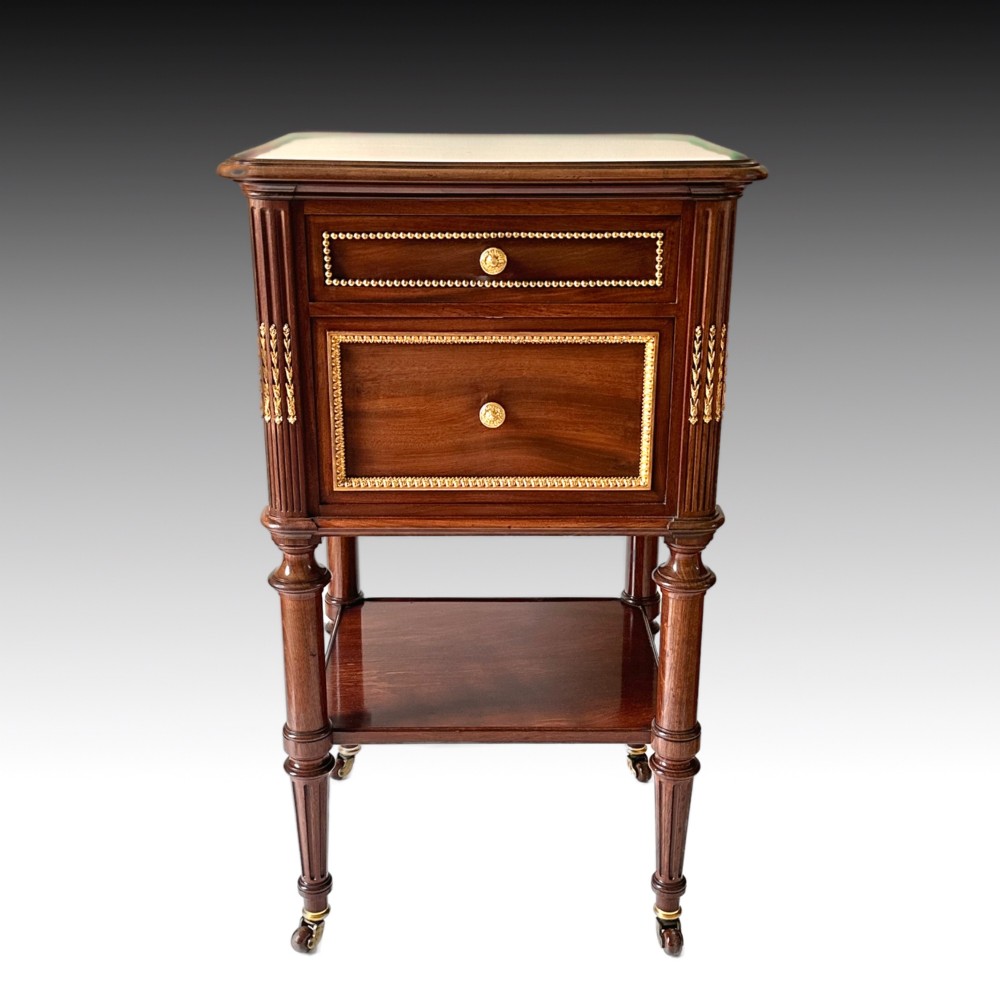 A French Louis XVI style mahogany bedside cabinet featuring two drawers framed with beaded ormolu trim, fluted corner columns, a lower tier shelf, and turned legs with brass castors. View VI